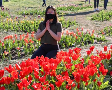 Faye with hands together at the heart surrounded by red flowers